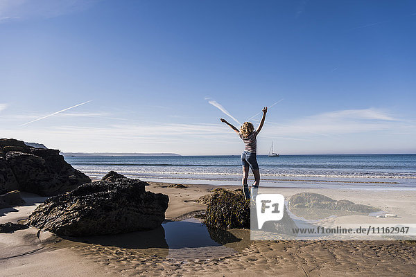 Frankreich  Halbinsel Crozon  Teenagermädchen auf dem Felsen am Strand stehend  Arme hebend