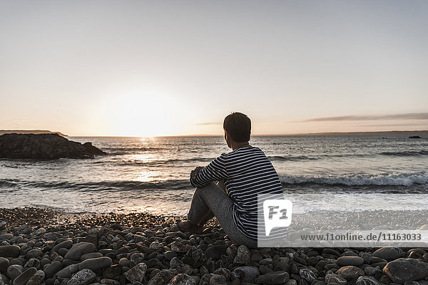 France  Bretagne  Crozon peninsula  woman sitting on stony beach at sunset