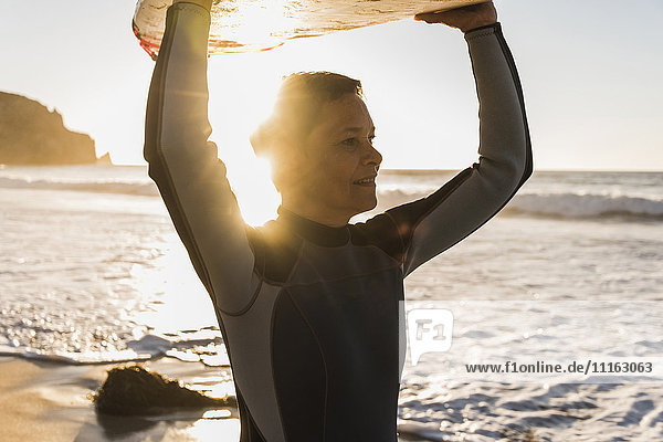 Frankreich Bretagne Halbinsel Crozon Frau am Strand bei Sonnenuntergang mit Surfbrett