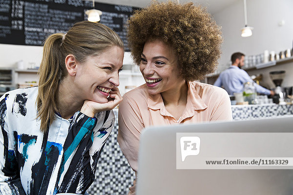 Two happy young women with laptop in a cafe