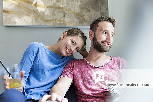 Lächelndes junges Paar auf der Couch sitzend mit Getränk