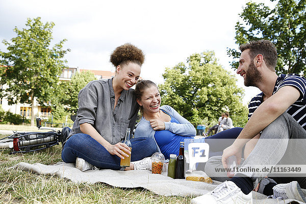 Three happy friends drinking in park
