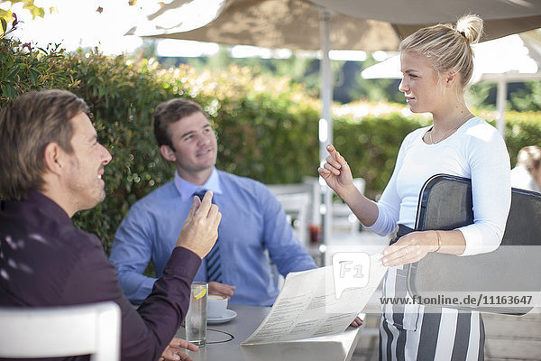 Kellnerin im Gespräch mit zwei Geschäftsleuten im Außenrestaurant