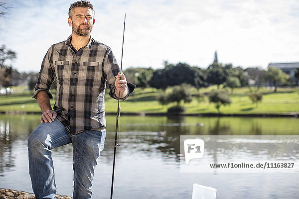 Mann mit Angelrute neben dem Teich