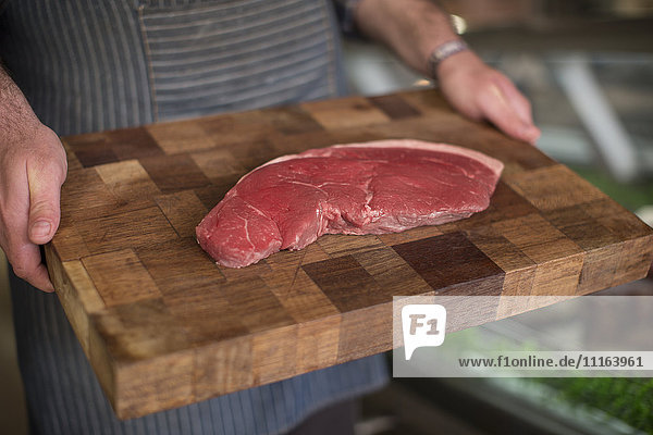 Butcher holding raw steak on wooden board