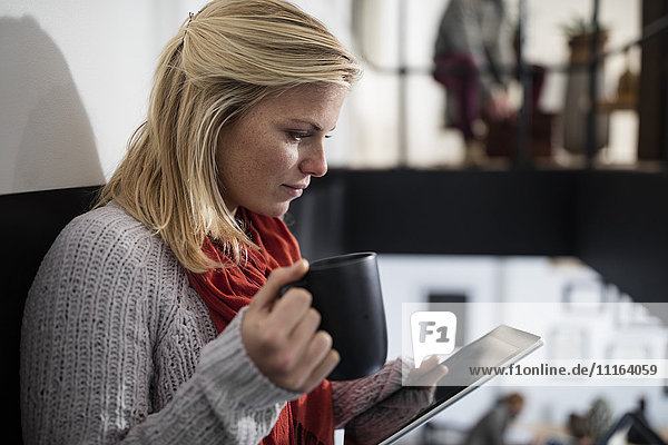 Junge Frau liest auf digitalem Tablett  Tasse Kaffee haltend