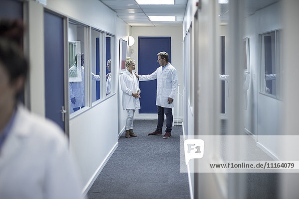 Man and woman in lab coats talking on corridor