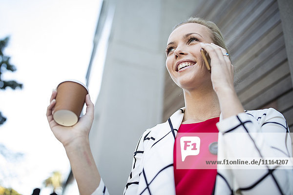 Lächelnde Frau mit Kaffee zum Mitnehmen am Handy