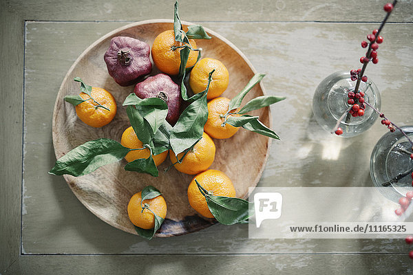 Eine Holzschale mit Orangen  Zitrusfrüchten auf einer Tischplatte.