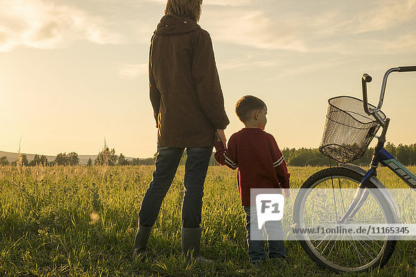 Mother and son holding hands in field near bicycle