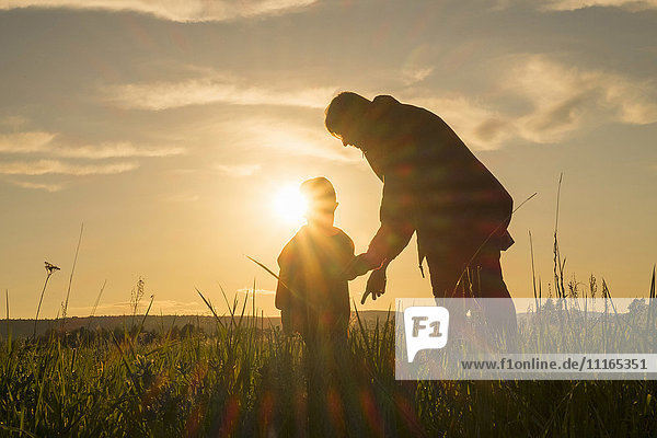 Frau und Sohn stehen bei Sonnenuntergang auf einem Feld