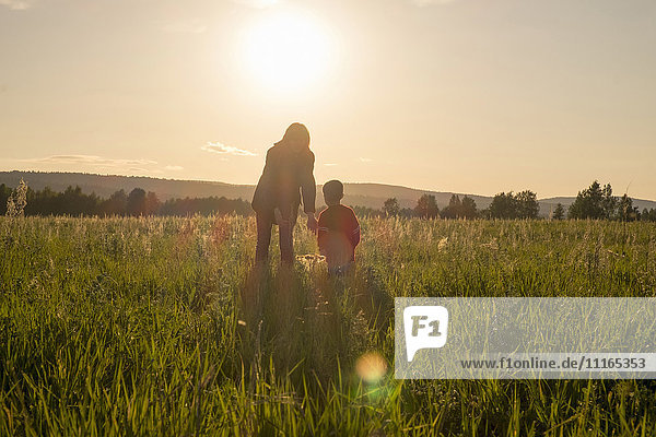 Woman and son standing in field at sunset