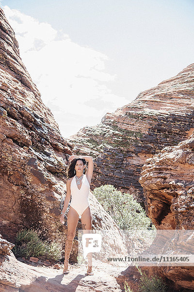 Junge Frau im weißen Badeanzug  die mit erhobenem Arm in einem Canyon-Tal steht.