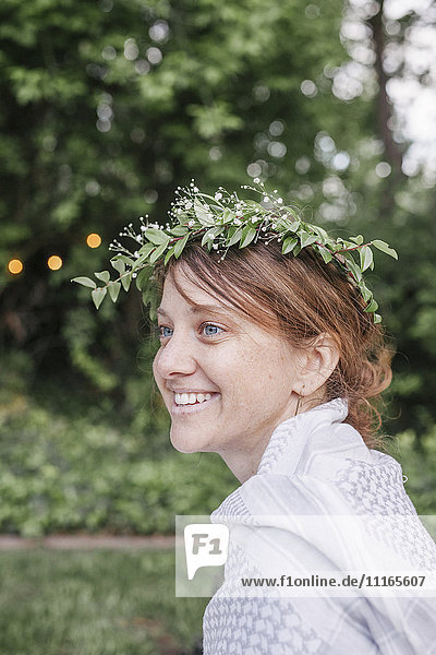 Smiling woman with a flower wreath in her hair sitting in a garden.