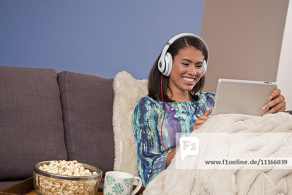 Lächelnde hispanische Frau auf dem Sofa sitzend mit digitalem Tablet