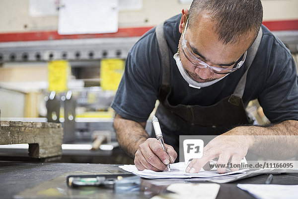 Hispanic worker writing on paperwork in factory