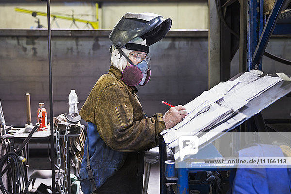 Asiatischer Arbeiter mit Maske schreibt in einer Fabrik auf Papiere