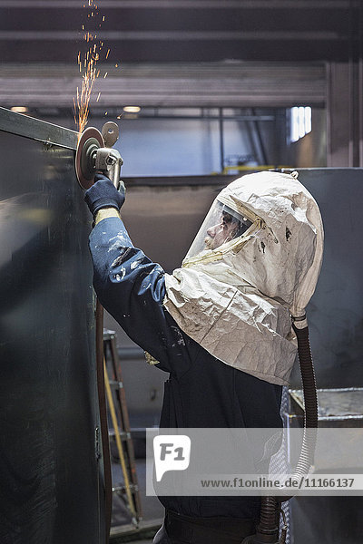 Caucasian worker grinding metal container in factory