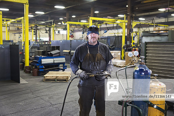 Caucasian welder posing with blowtorch in factory