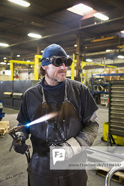 Caucasian welder holding blowtorch in factory