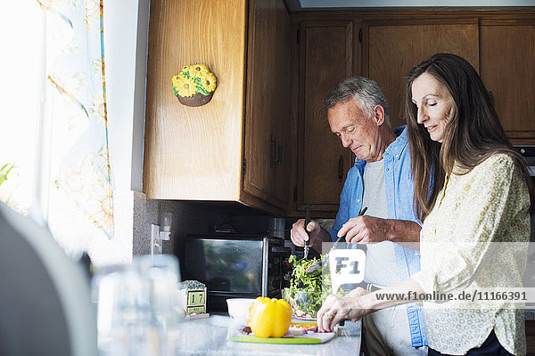 Lächelndes älteres Paar  das in einer Küche steht und Essen zubereitet.