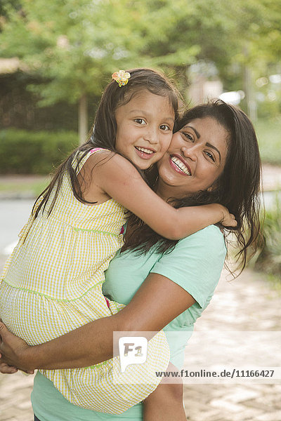 Hispanische Mutter  die ihre Tochter trägt und umarmt