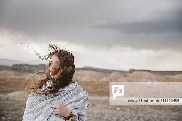 Eine Frau mit langen Haaren  die im Wind weht und in einer Wüstenlandschaft steht.