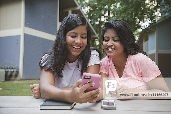 Hispanische Mutter und Tochter telefonieren in der Nähe von Wohnungen mit ihrem Handy