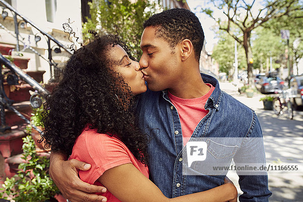 Lächelndes Paar küsst sich auf dem Bürgersteig der Stadt