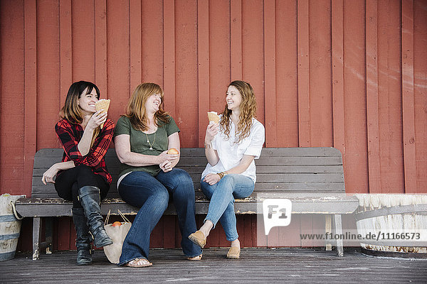 Drei Frauen sitzen auf einer Bank und essen Eiscreme.