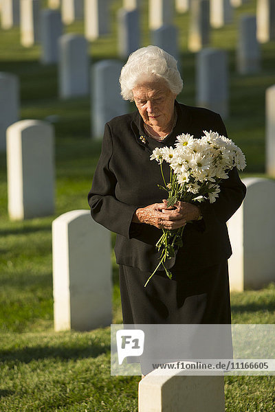 Caucasian widow holding bouquet at cemetery gravestone