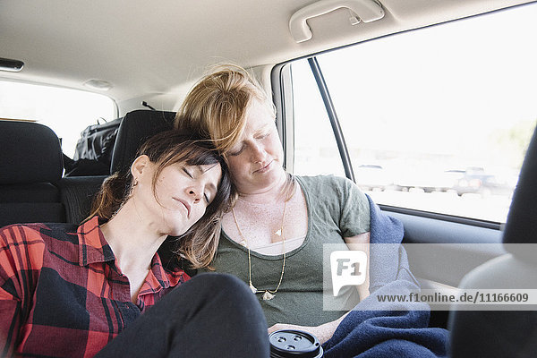 Two women in a car on a road trip  both asleep in the back seat  heads together.