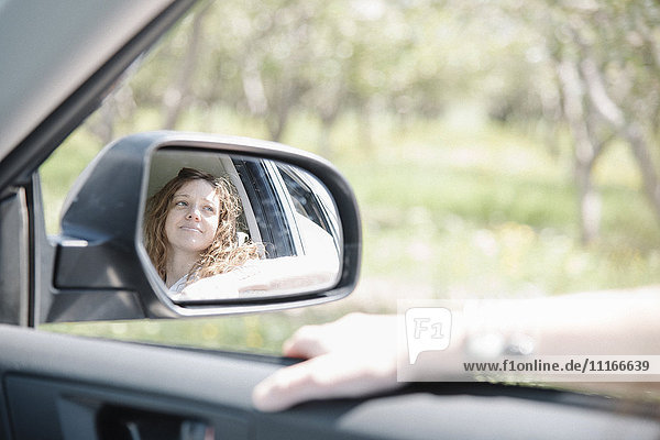 Frau im Auto auf einer Autofahrt  Blick aus dem Fenster  Spiegelung im Seitenspiegel gesehen.