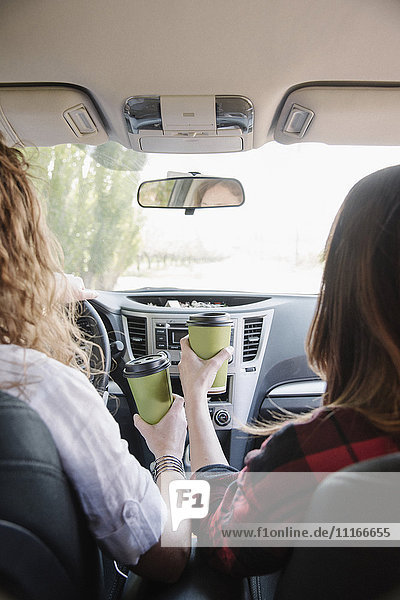 Two women in a car holding coffee cups. View over shoulder.