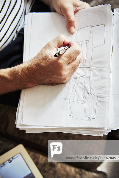 Ein Mann  der mit einer Feder sitzt und Skizzen zeichnet  ein Designer bei der Arbeit.