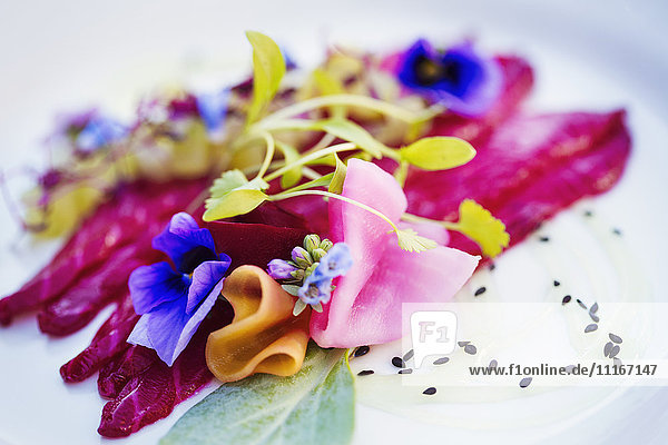Carpaccio und Garnierung aus frischen Erbsensprossen und essbaren Blüten auf einem weißen Teller. .
