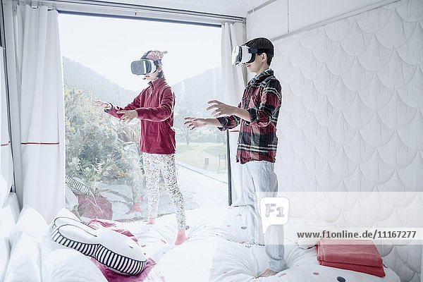 Mixed Race brother and sister using virtual reality goggles on bed