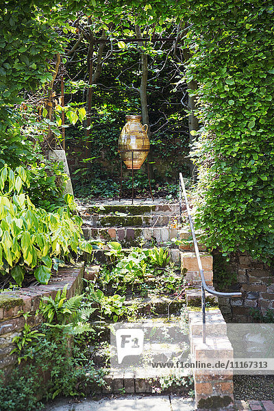 A glazed or amphora in a frame on a terrace at the top of steps  under a pergola.