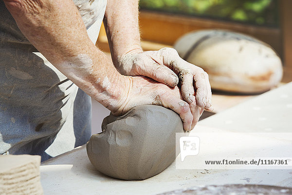 A person  potter preparing a lump of damp clay for throwing.