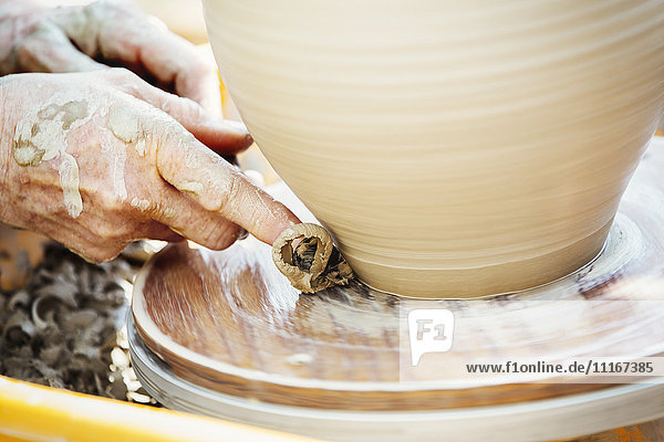 A woman potter working clay on a potter's wheel in her workshop.