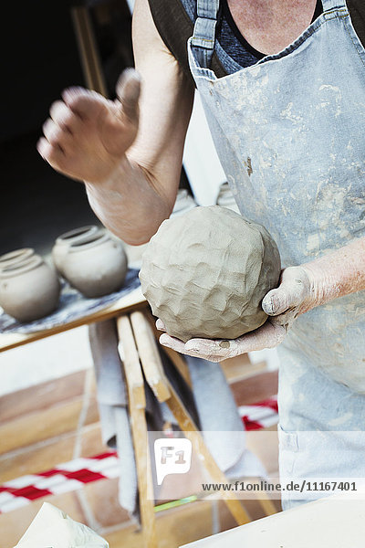 A potter handling a ball of wet clay pot  moulding and working it.