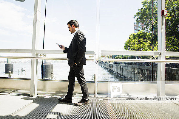 Geschäftsmann in einem grauen Anzug  der im Freien steht und sein Mobiltelefon benutzt.