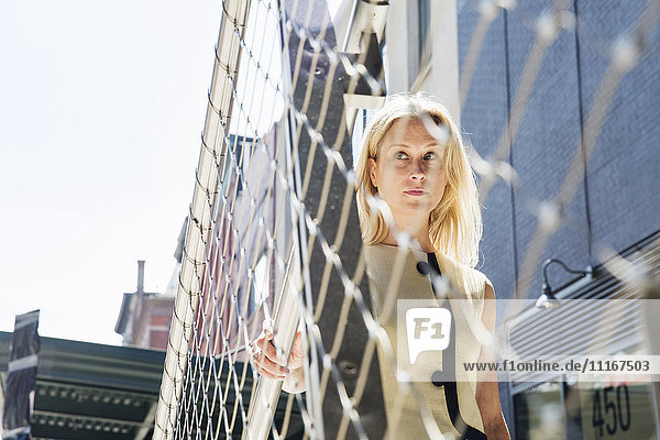 Geschäftsfrau  die an einem Metalldrahtzaun in New York steht.