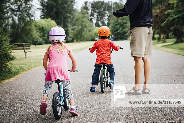 Father watching daughter and son riding bicycles