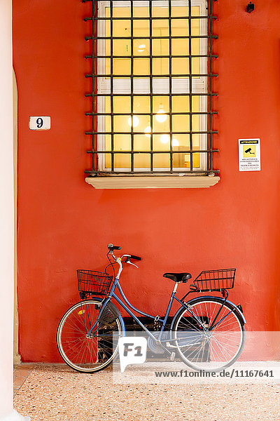 Blaues Fahrrad lehnt an orangefarbener Wand unter Fenster