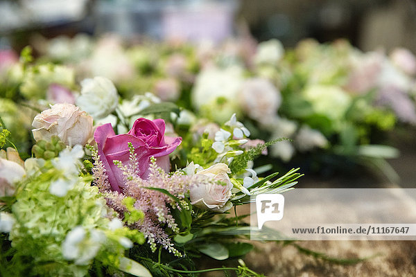 Nahaufnahme von Arrangements auf einer Werkbank. Rosa und weiße Blumen mit grünem Laub.