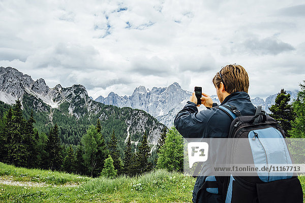 Kaukasischer Mann  der mit seinem Mobiltelefon ein Gebirge fotografiert