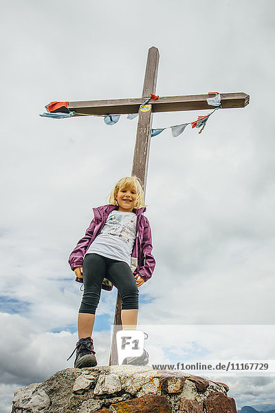 Kaukasisches Mädchen posiert auf einem Felsen vor einem Kruzifix