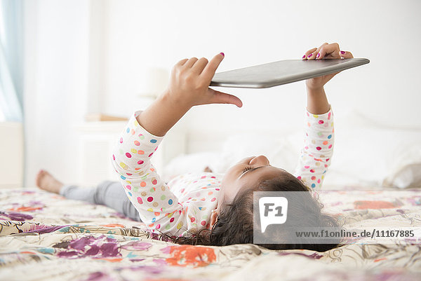 Gemischtrassiges Mädchen auf dem Bett liegend mit digitalem Tablet