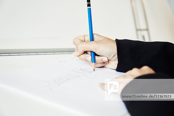 Eine Frau arbeitet an einer Grafik auf einem Zeichenbrett und umreißt Buchstaben mit einem Bleistift.